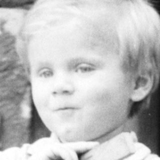 Black and white photo of a young boy standing outside.