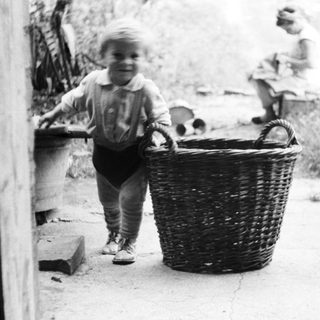 Child stands near a basket, woman sits nearby.