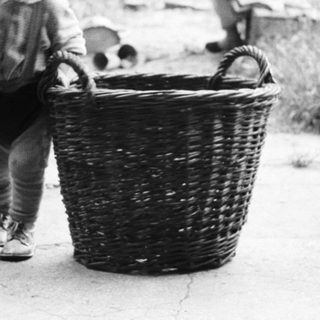 Child stands near a basket, woman sits nearby.