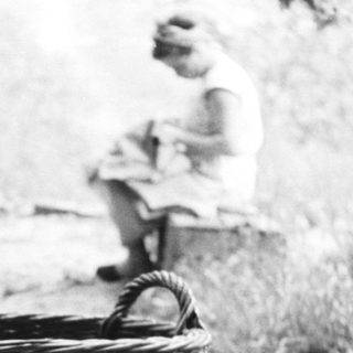 Child stands near a basket, woman sits nearby.