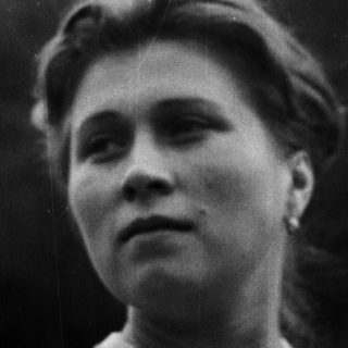 Here's a brief summary of the image: Woman in sweater stands outdoors, looking upwards.