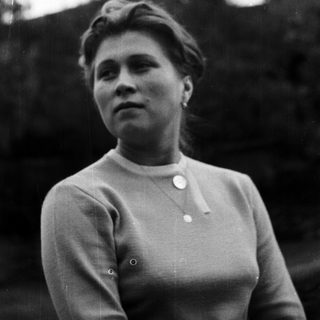 Here's a brief summary of the image: Woman in sweater stands outdoors, looking upwards.