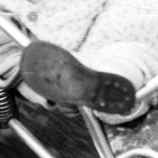 Here's a brief summary of the image: Baby sits in a vintage stroller outdoors.