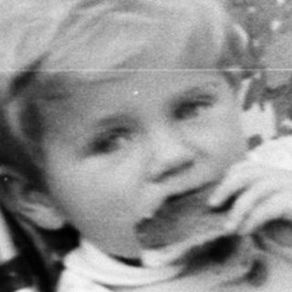 Here's a brief summary of the image: Baby sits in a vintage stroller outdoors.