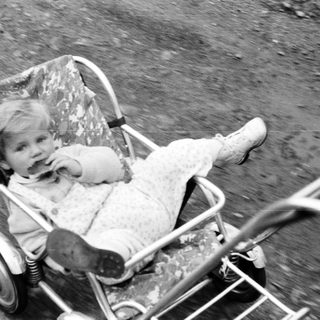 Here's a brief summary of the image: Baby sits in a vintage stroller outdoors.