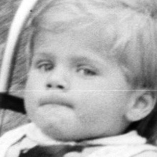Baby seated in a vintage wheeled stroller outdoors.