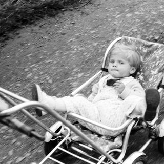 Baby seated in a vintage wheeled stroller outdoors.