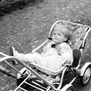 Baby seated in a vintage wheeled stroller outdoors.