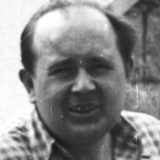 Man in plaid shirt leans against stone steps.