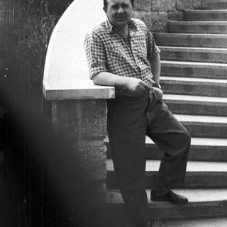 Man in plaid shirt leans against stone steps.