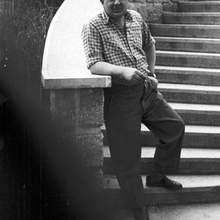 Man in plaid shirt leans against stone steps.
