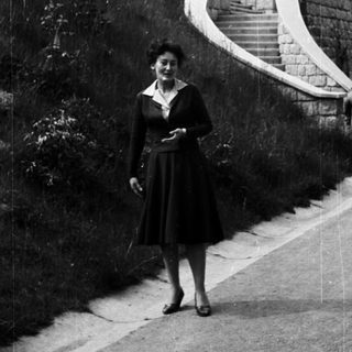 Woman stands on road with stairs and greenery behind.