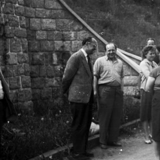 Group of people standing near a stone wall and road.