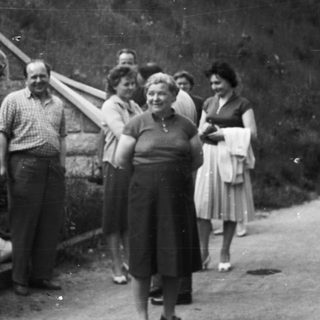 Group of people standing near a stone wall and road.