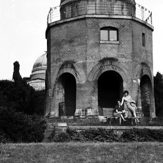 People seated near a brick tower with arches.