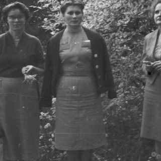 Three women stand outdoors, appearing formal and posed.