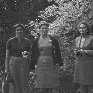 Three women stand outdoors, appearing formal and posed.