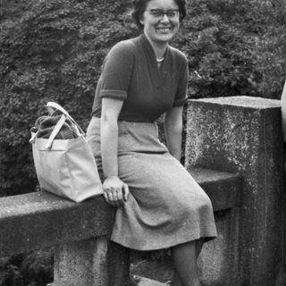 Woman sits on a stone bridge, holding a bag.