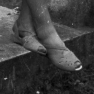 Woman sits on a stone bridge, holding a bag.
