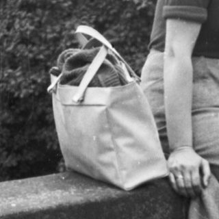 Woman sits on a stone bridge, holding a bag.