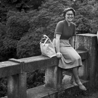 Woman sits on a stone bridge, holding a bag.