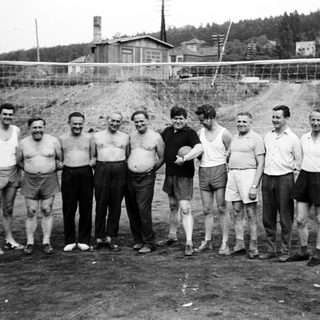 Group of men stand near a volleyball net.