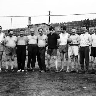 Group of men pose near a volleyball net outdoors.