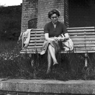 Woman sits on a bench near an archway.