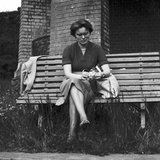 Woman sits on a bench near an archway.