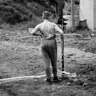 Here's a brief summary of the image: Two boys climbing a utility pole in a rural area.