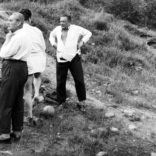 Two men stand near another, outdoors in a grassy area.