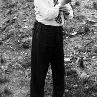 Man in suit gestures in a hillside landscape.