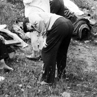 Men examining wreckage in a grassy, hillside area.