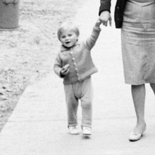 Woman walks with child on a tree-lined path.