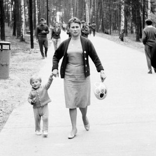 Woman walks with child on a tree-lined path.