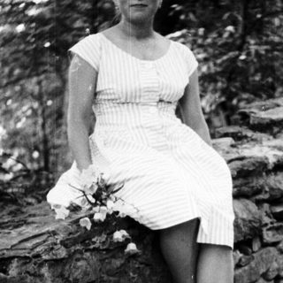Woman in dress sits on stone wall outdoors.