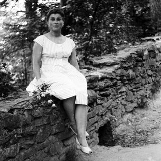 Woman in dress sits on stone wall outdoors.