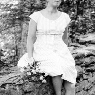 Here's a brief summary of the image: Woman in dress sits on a stone wall outdoors.