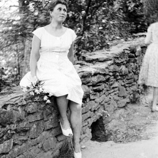 Here's a brief summary of the image: Woman in dress sits on a stone wall outdoors.
