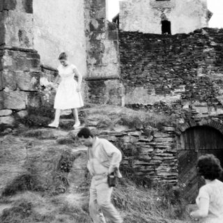 People explore stone ruins on a grassy hillside.