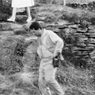 People explore stone ruins on a grassy hillside.