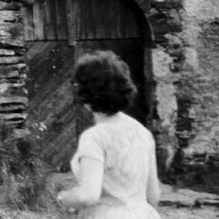 People explore stone ruins on a grassy hillside.
