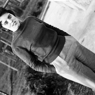 Black and white portrait of a person in a sweater and pants.
