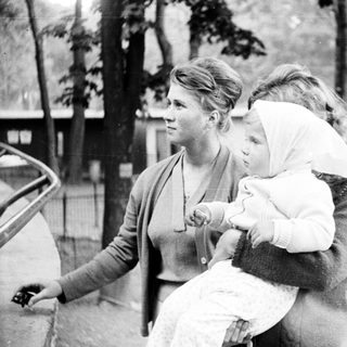Woman holds baby while standing outdoors, appearing thoughtful.