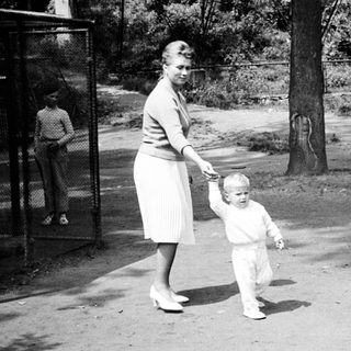 Woman and toddler walk outdoors; others are in background.