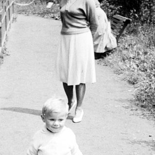 Here's a brief summary of the image: Child walks along a path, with an adult nearby.