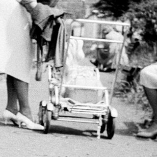 A child walks past adults and a stroller.