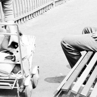 Man sits on a bench, smoking, with a scooter nearby.