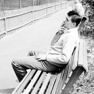 Man sits on a bench, smoking, with a scooter nearby.