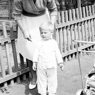 Mother and young child stand near a fence.